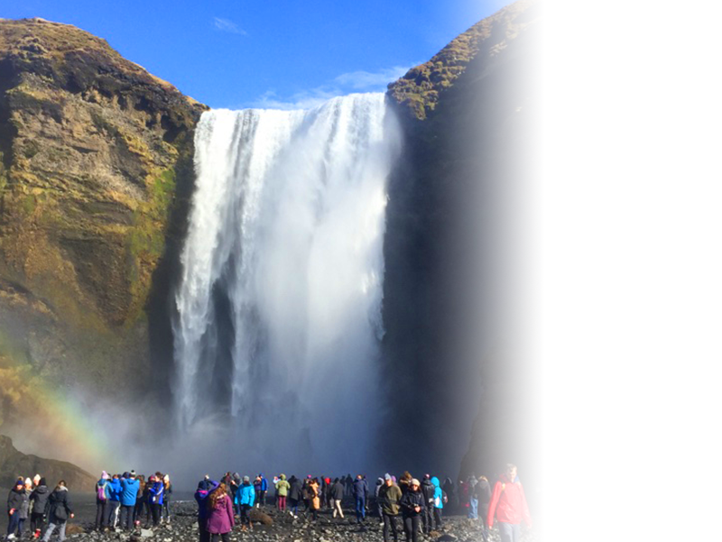 Image shows a group of people standing at the bottom of Skogafoss waterfall, in Iceland