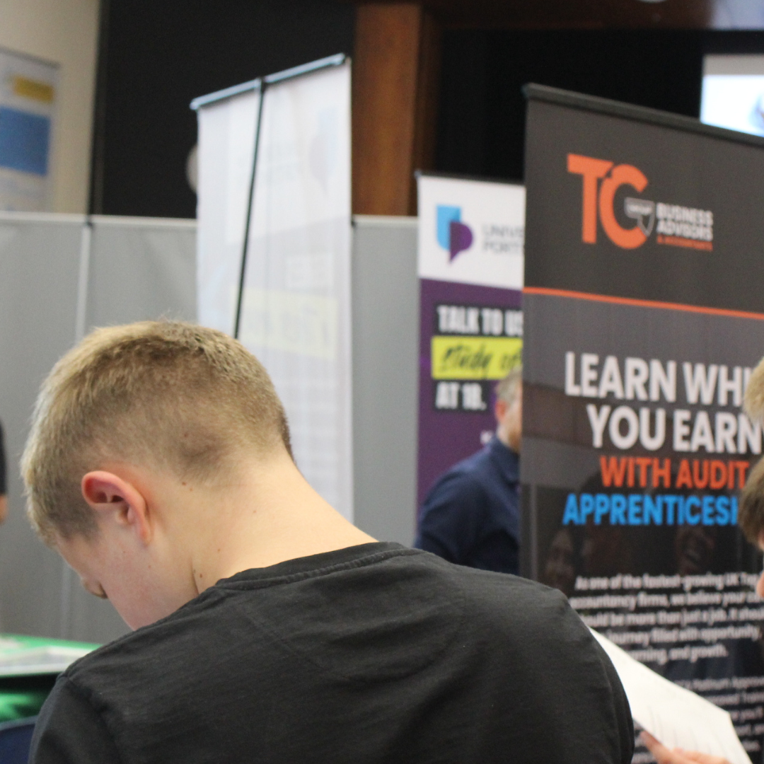 A pupil reading information in front of a TC Group Business Advisors and Accountants display banner.