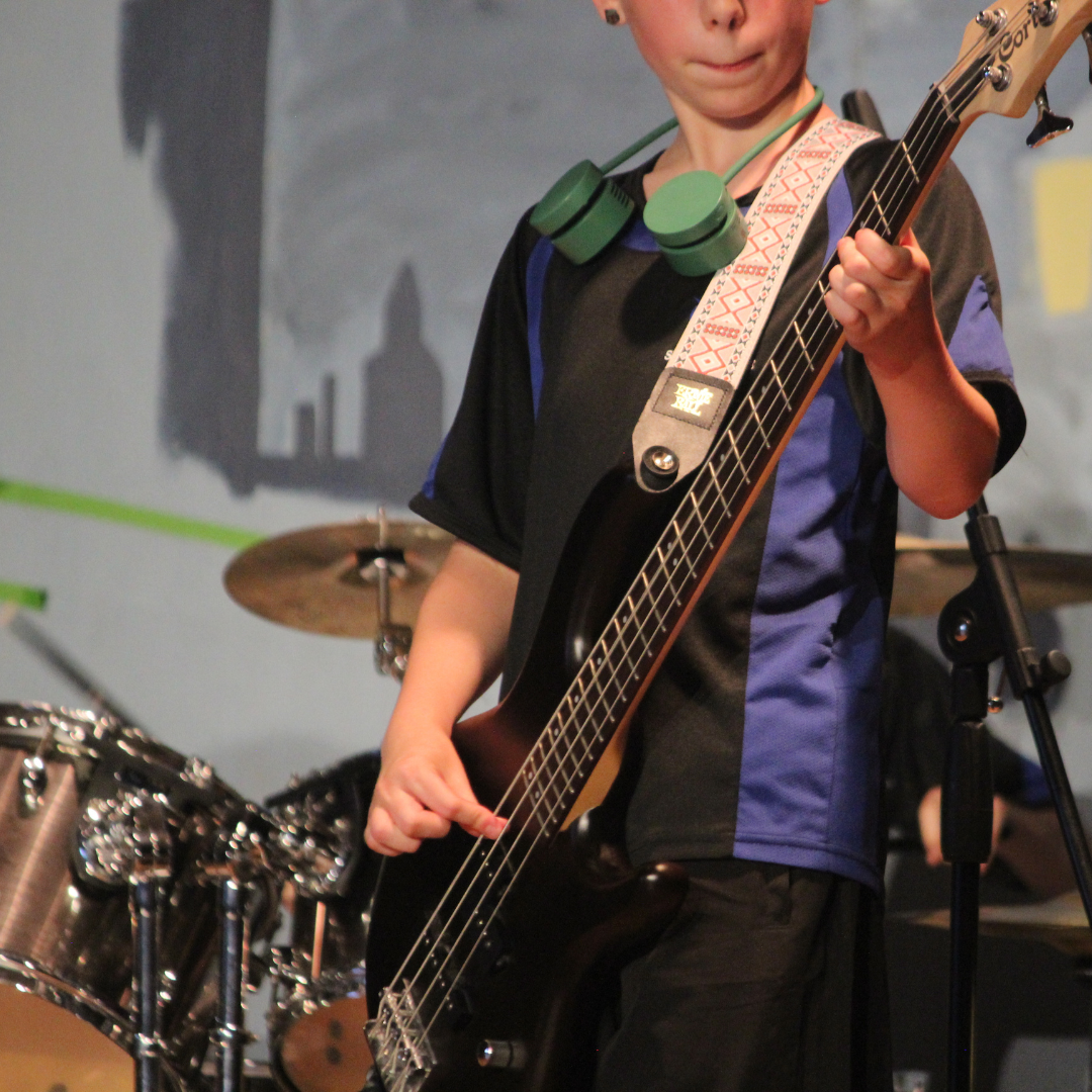 image shows a pupil dressed in PE kit playing an electric bass guitar