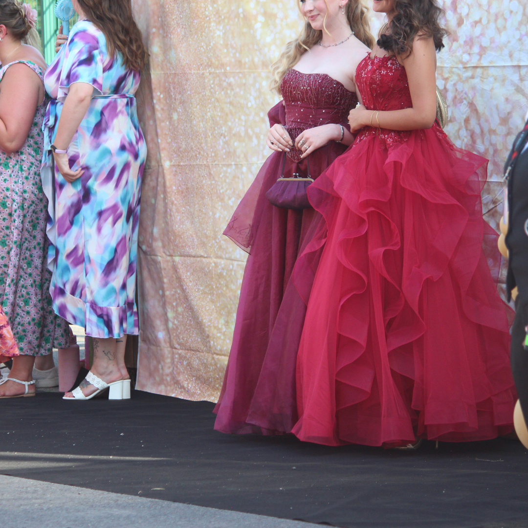 Two pupils in burgundy formal dresses posing together for a photograph.