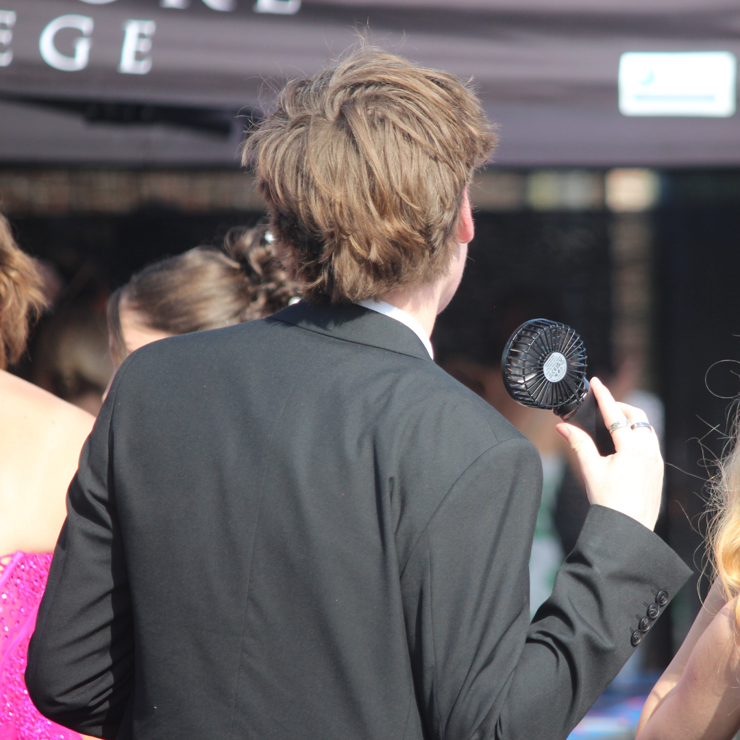 Pupil holding a handheld fan while standing with other pupils in formal wear.