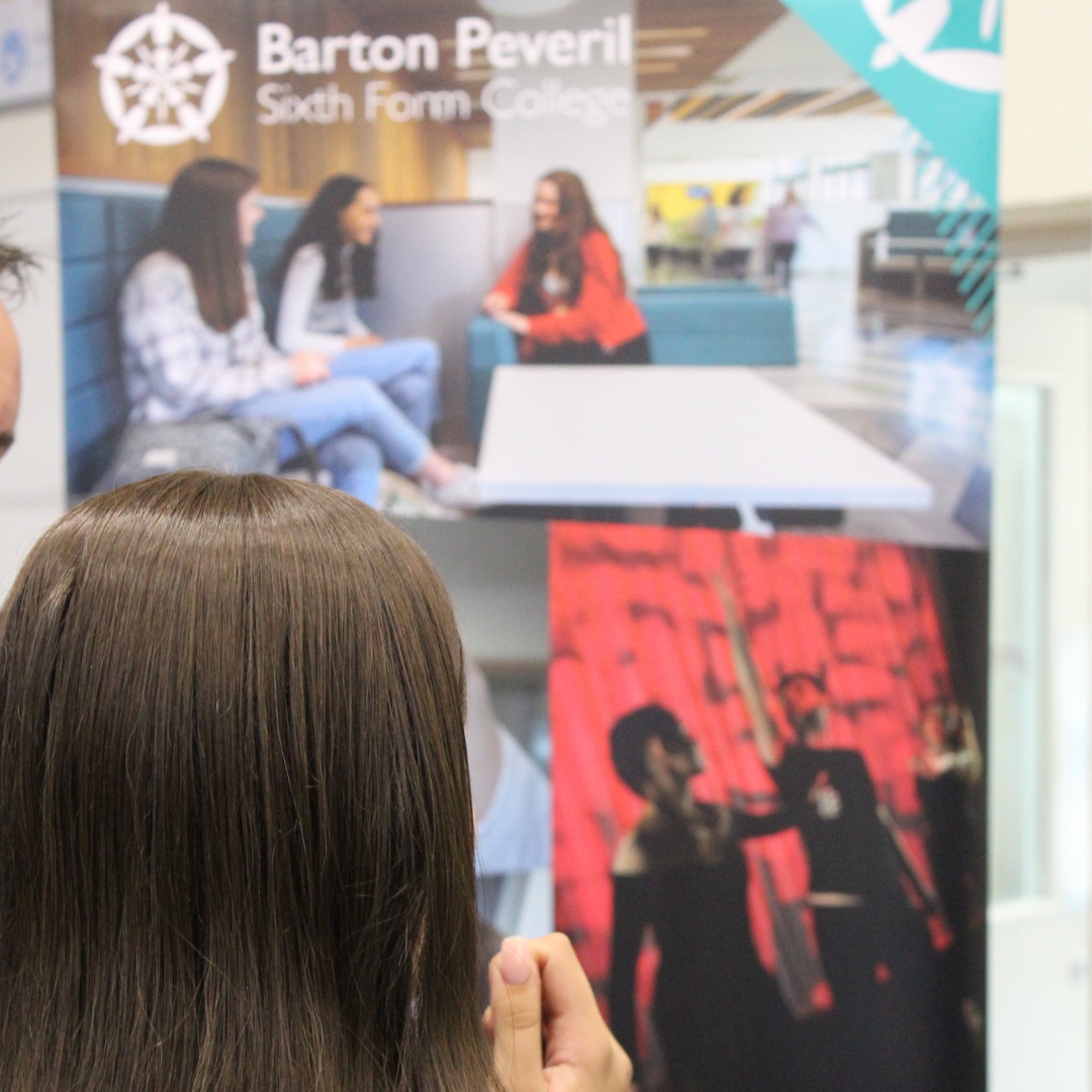 A pupil viewed from behind examining a exhibition banner for Barton Peveril Sixth Form College.