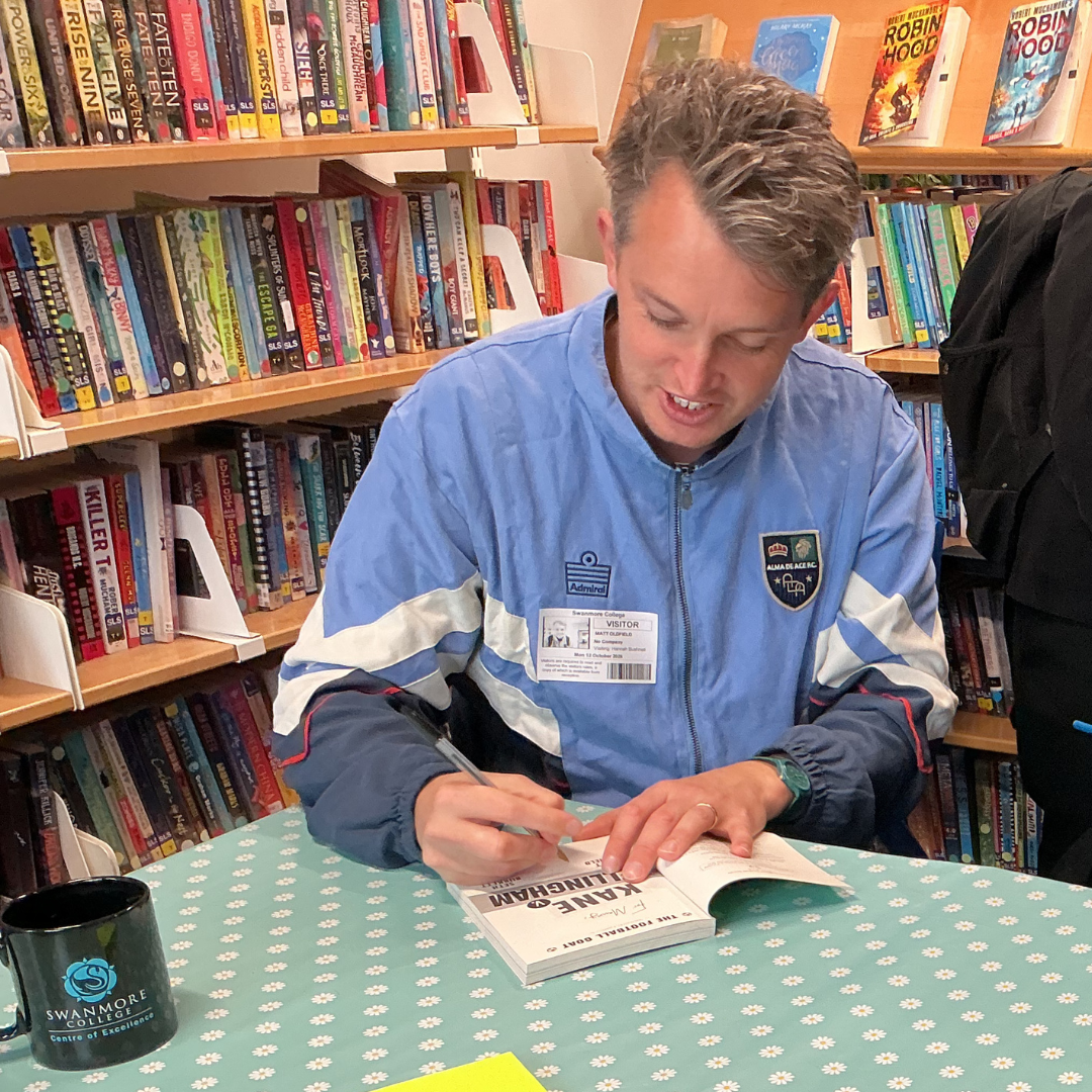 Author Matt Oldfield signing a copy of his book "Kane v. Bellingham" at a table in the library during his visit to Swanmore College.