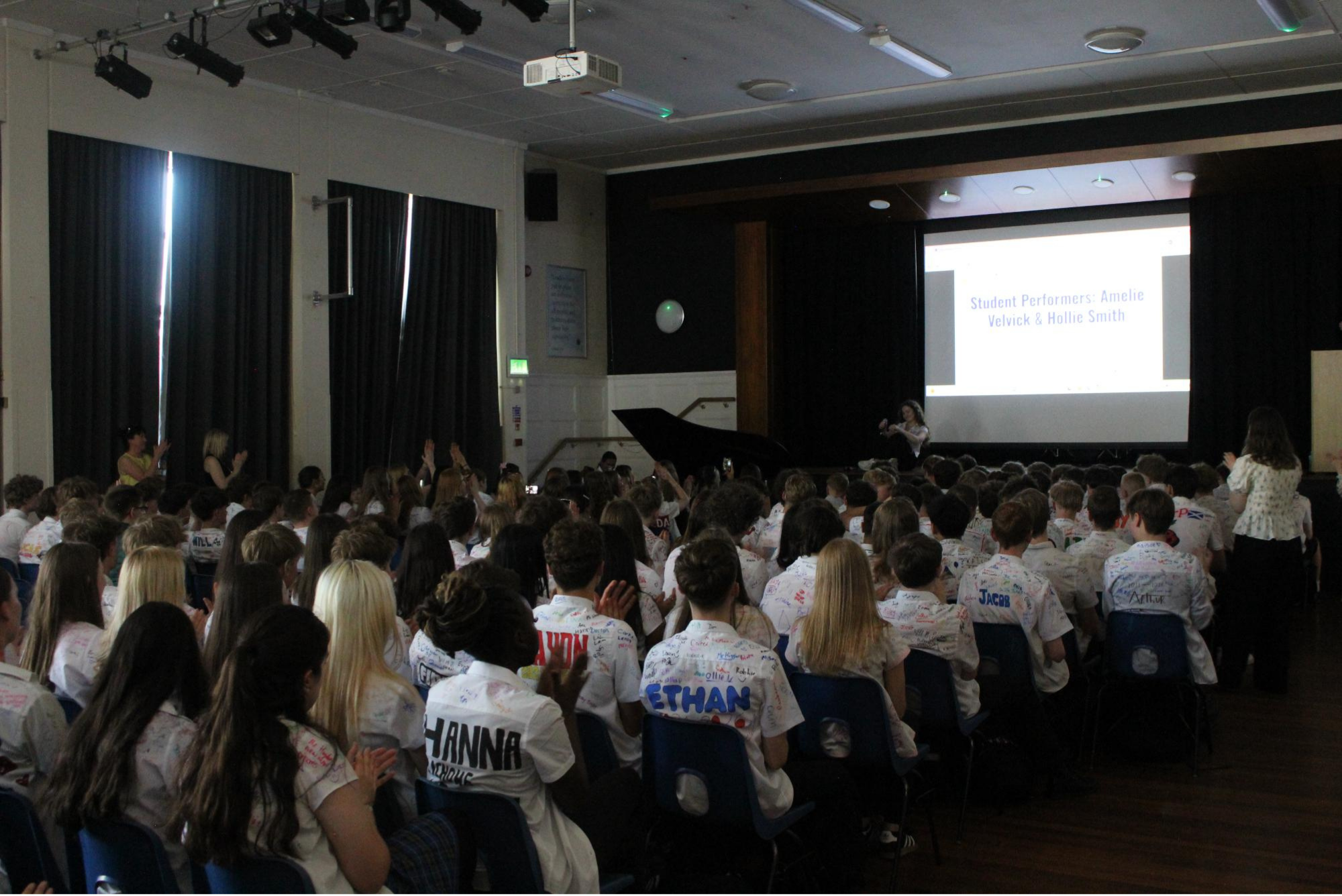 Year 11 pupils seated in the hall during a leavers' assembly, wearing shirts covered in messages and signatures.