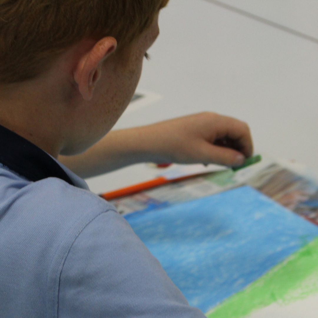 Image shows a pupil using pastels to colour in a page