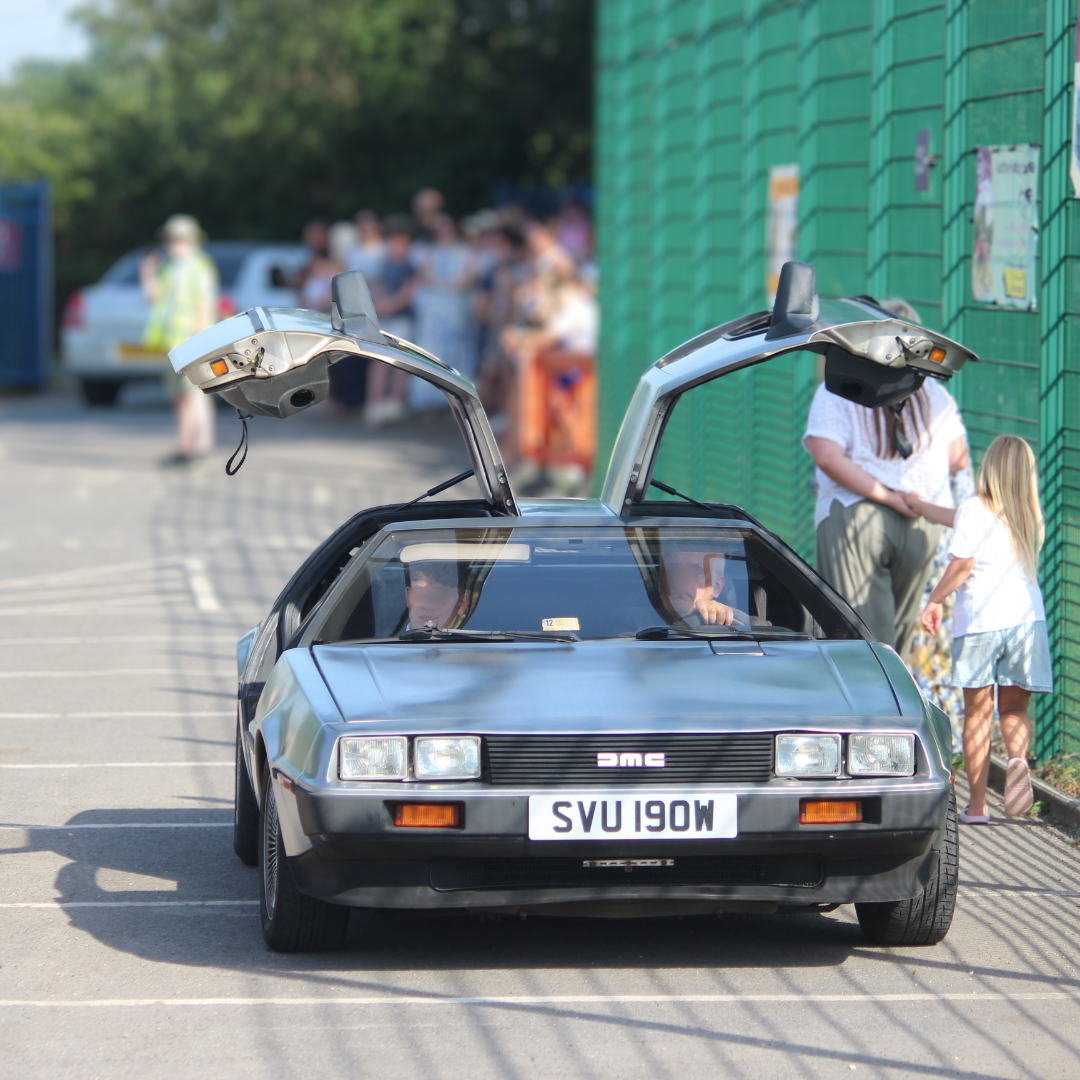 A silver DeLorean with gullwing doors open arriving at the prom.