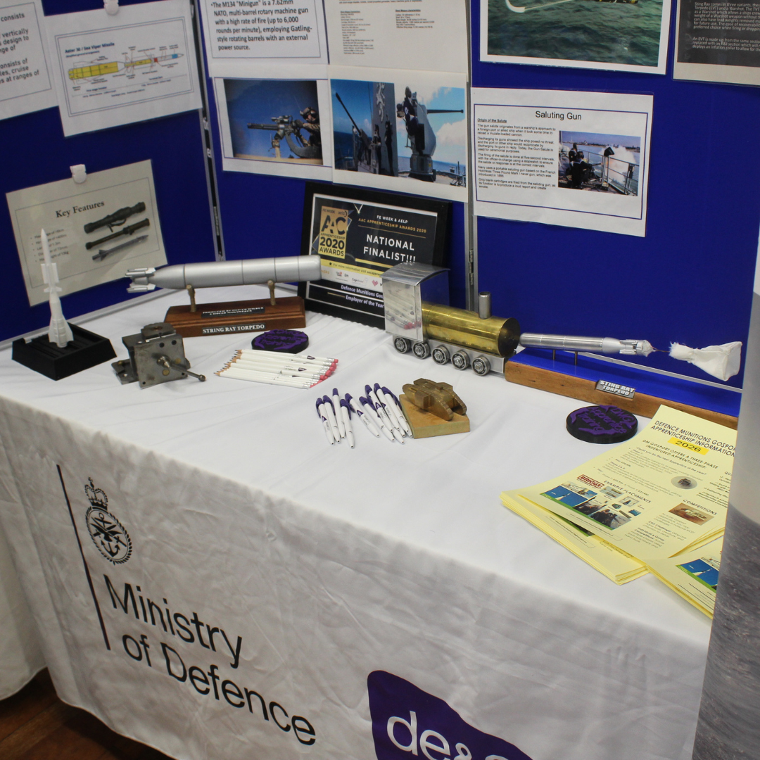 A Ministry of Defence display table showcasing various military models, promotional items, and information sheets for Defence Munitions Gosport Apprenticeships.