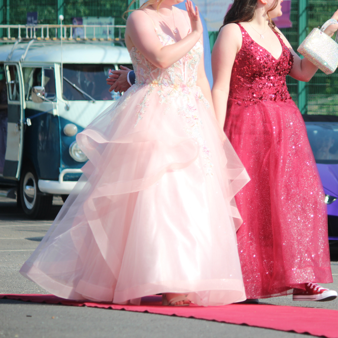 Two pupils in formal dresses standing on the red carpet.