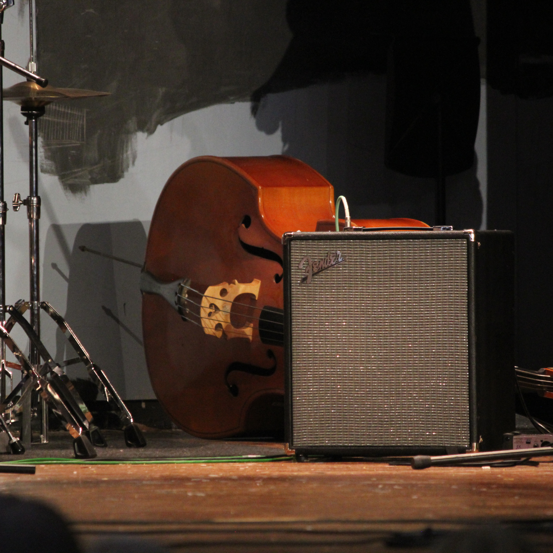 image shows a cello lying on its side behind and amplifier on stage