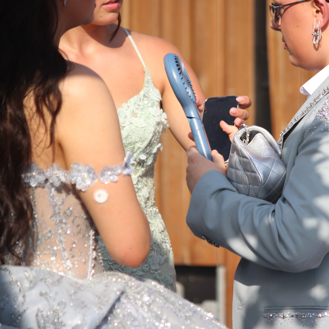 Pupils in formal attire using a handheld fan while standing together outdoors.