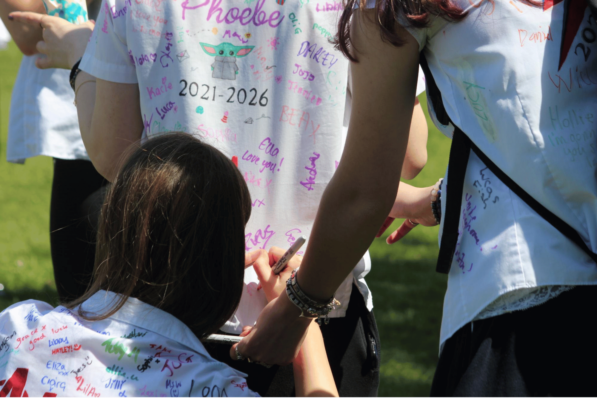 Pupil signs a classmate's shirt during Year 11 leavers' celebrations on the College field.