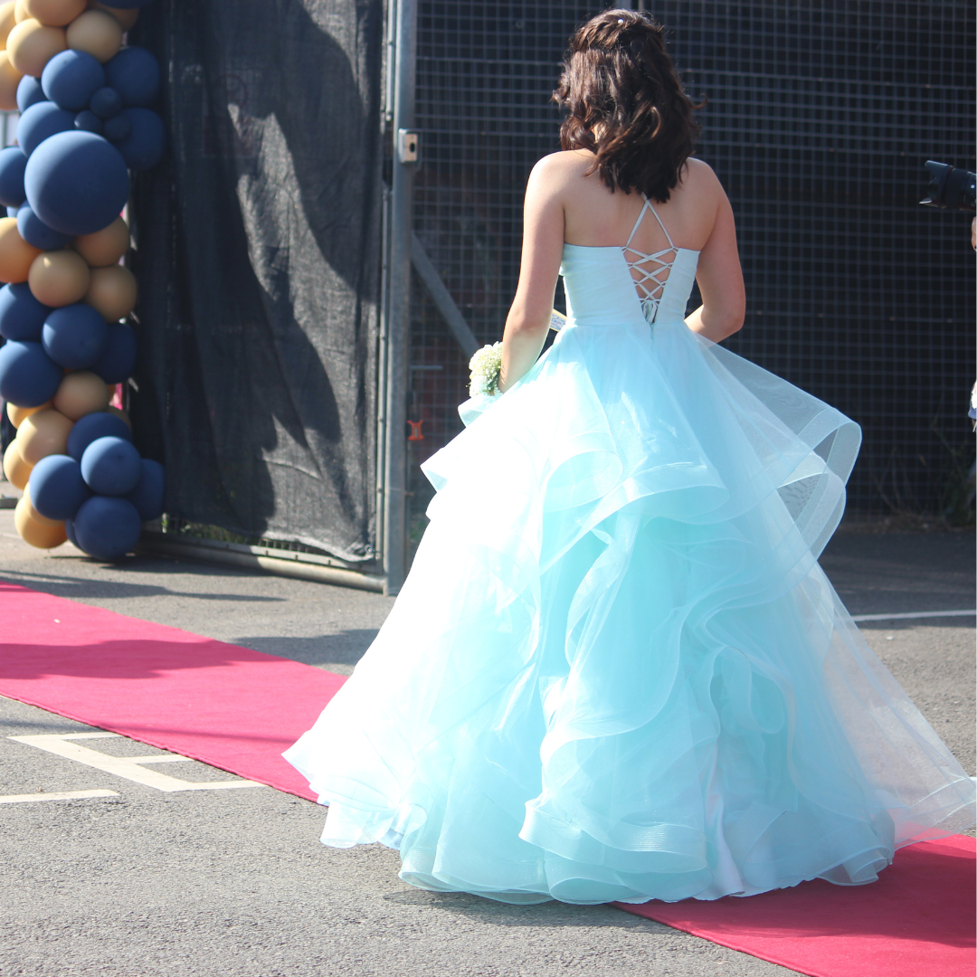 Rear view of a pupil in a light blue ballgown walking along the red carpet.