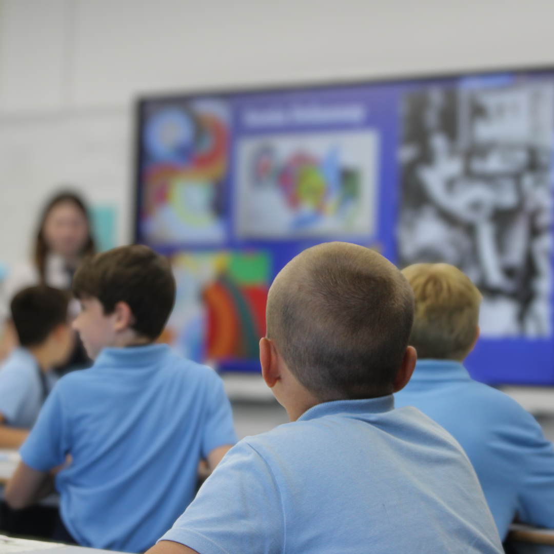 Image shows a group of primary school pupils listening to a presentation about art in a classroom.