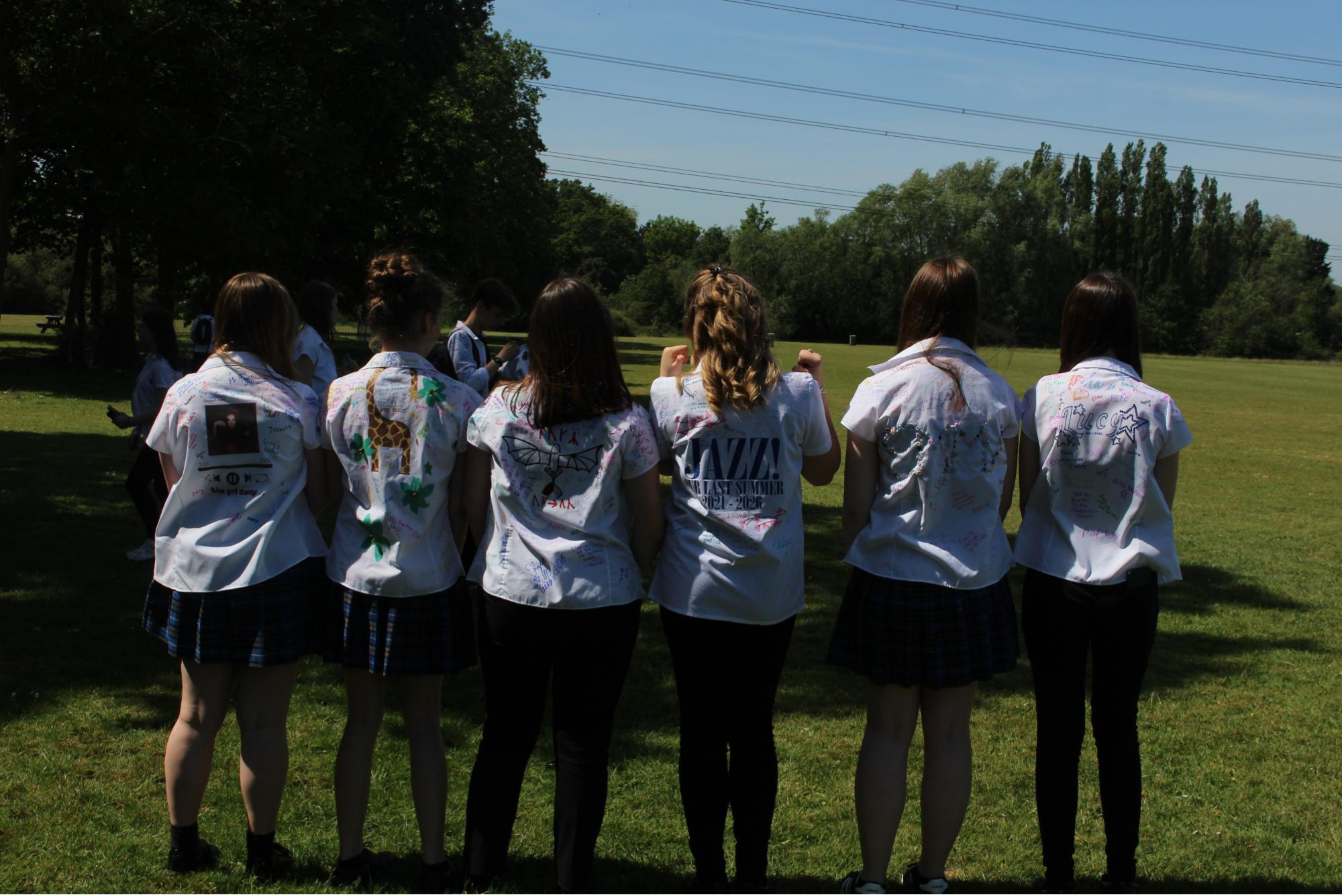 Group of Year 11 pupils standing together on the field, showing the decorated backs of their signed school shirts.
