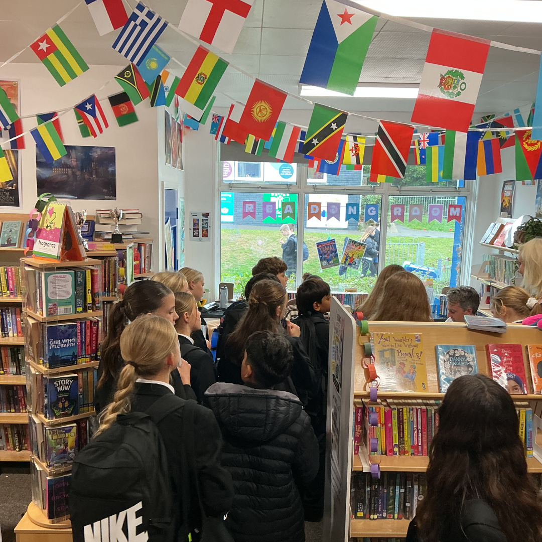 A line of pupils waiting in the school library under international flag bunting during a book signing session with author Matt Oldfield.