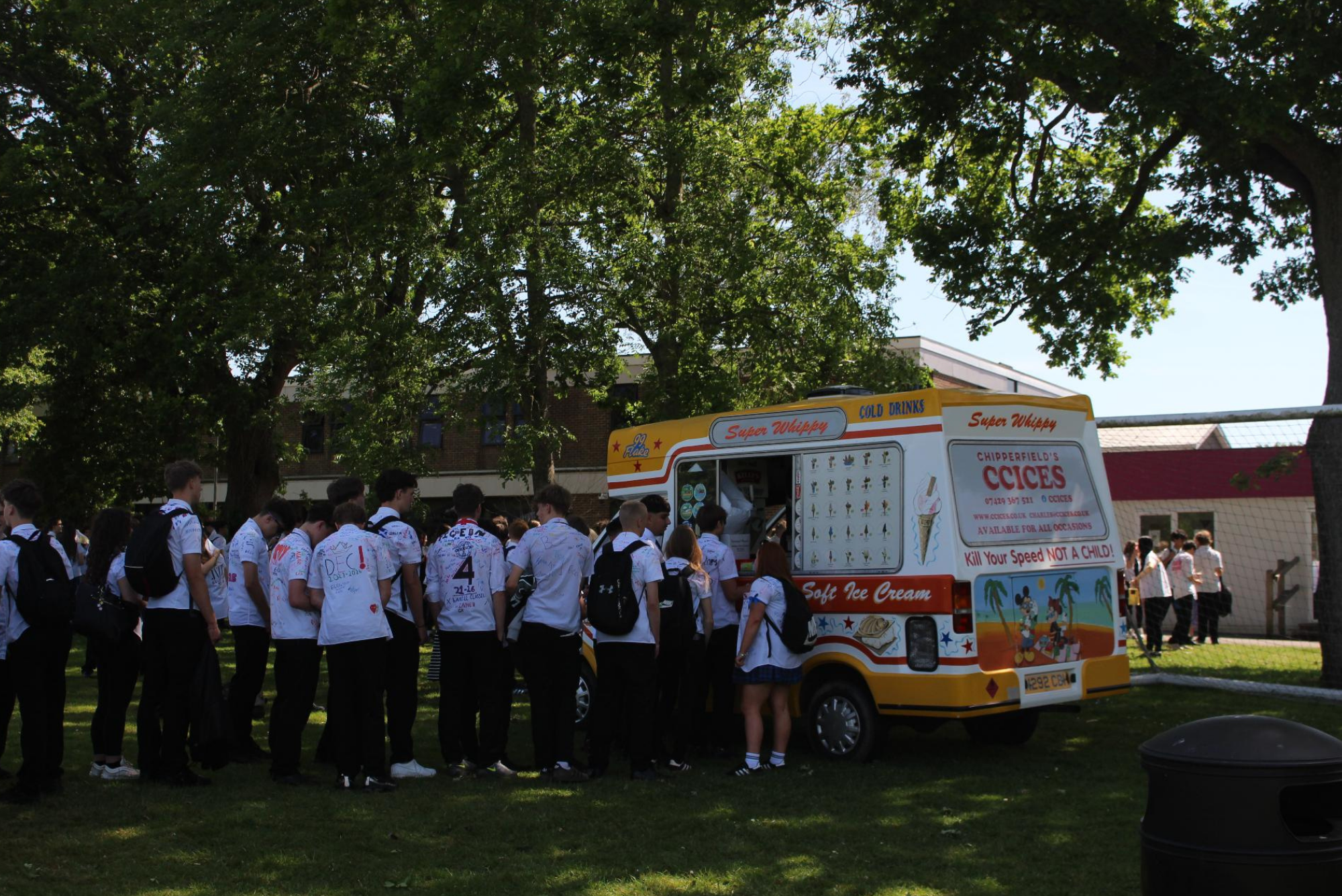 Year 11 pupils queue for ice cream from an ice cream van on the College field during leavers' celebrations.