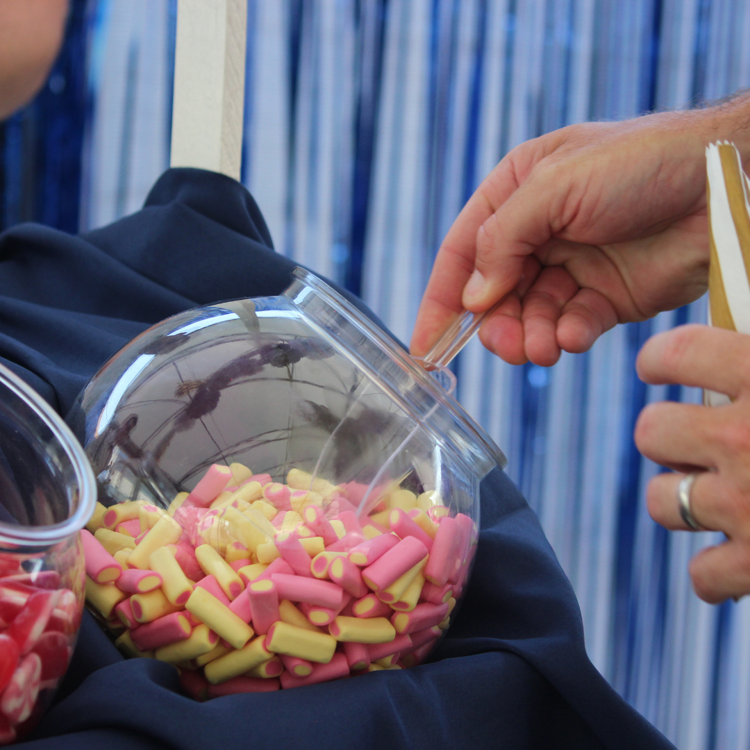 Hand using tongs to take sweets from a clear container.