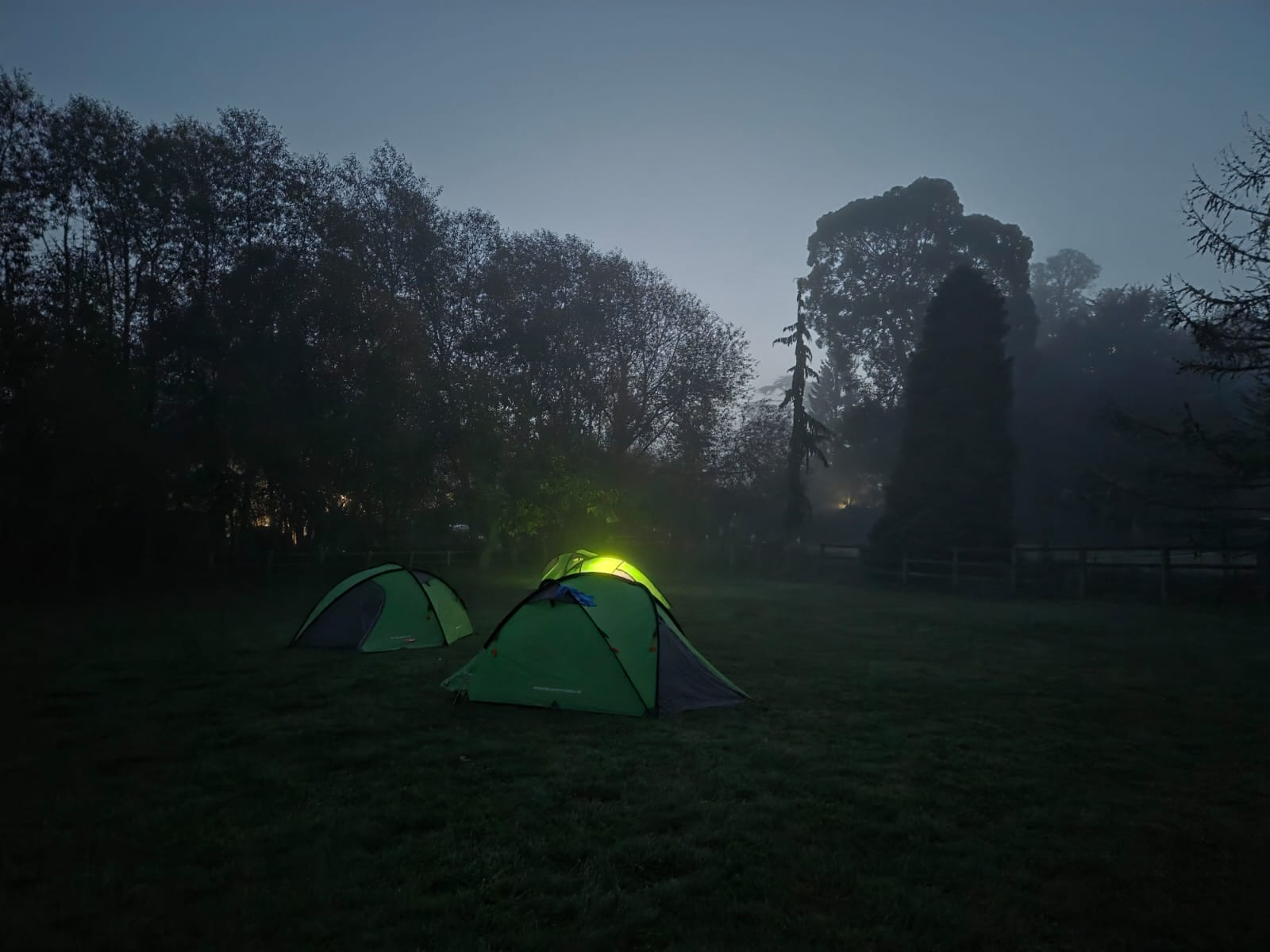 A campsite scene at dusk featuring pitched tents with one illuminated from within
