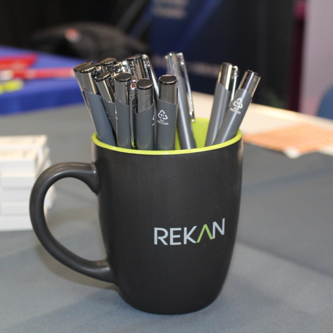 A black mug holding branded pens on a table at the Rekan exhibition stand.