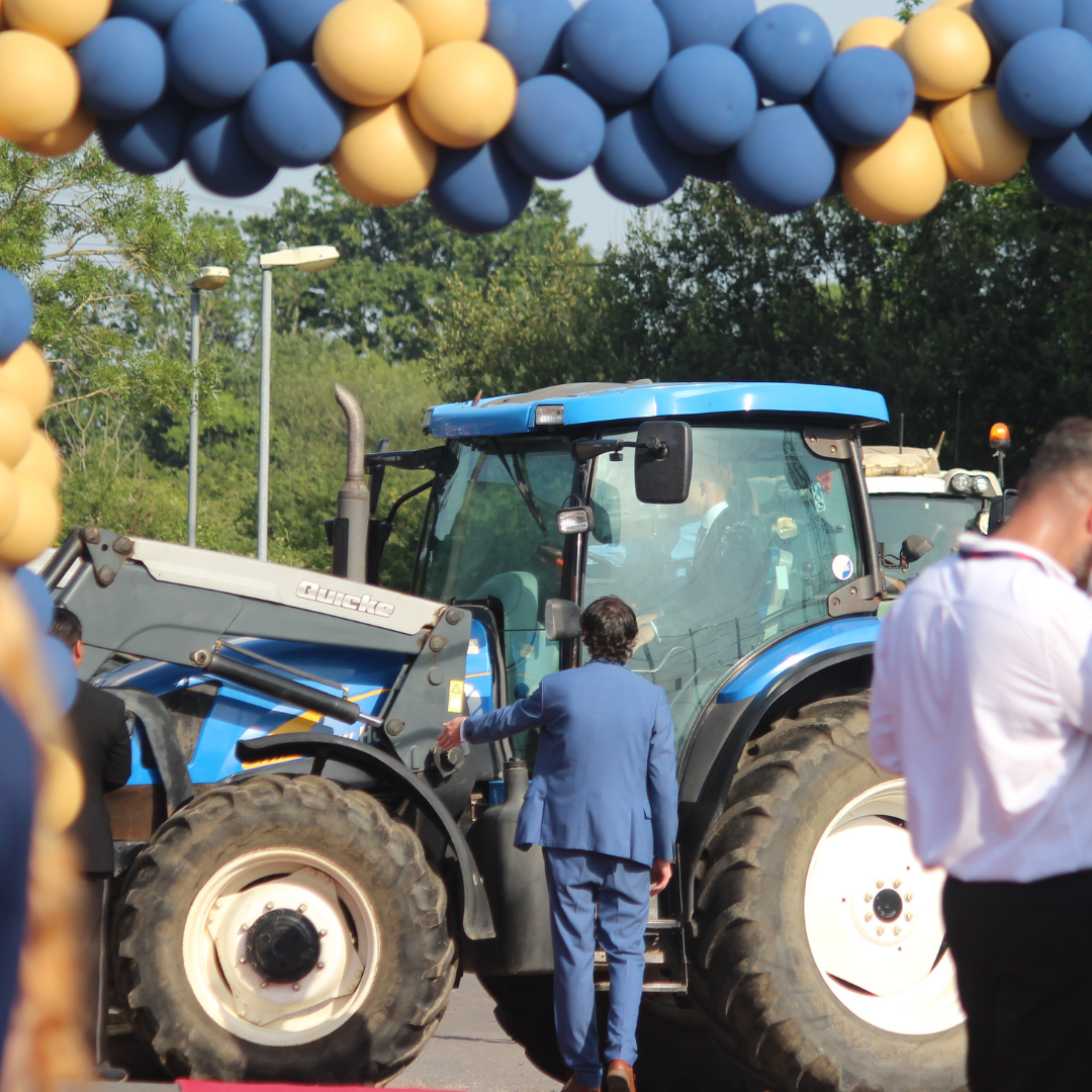 Blue tractor arriving beneath a blue and gold balloon arch at the prom entrance.