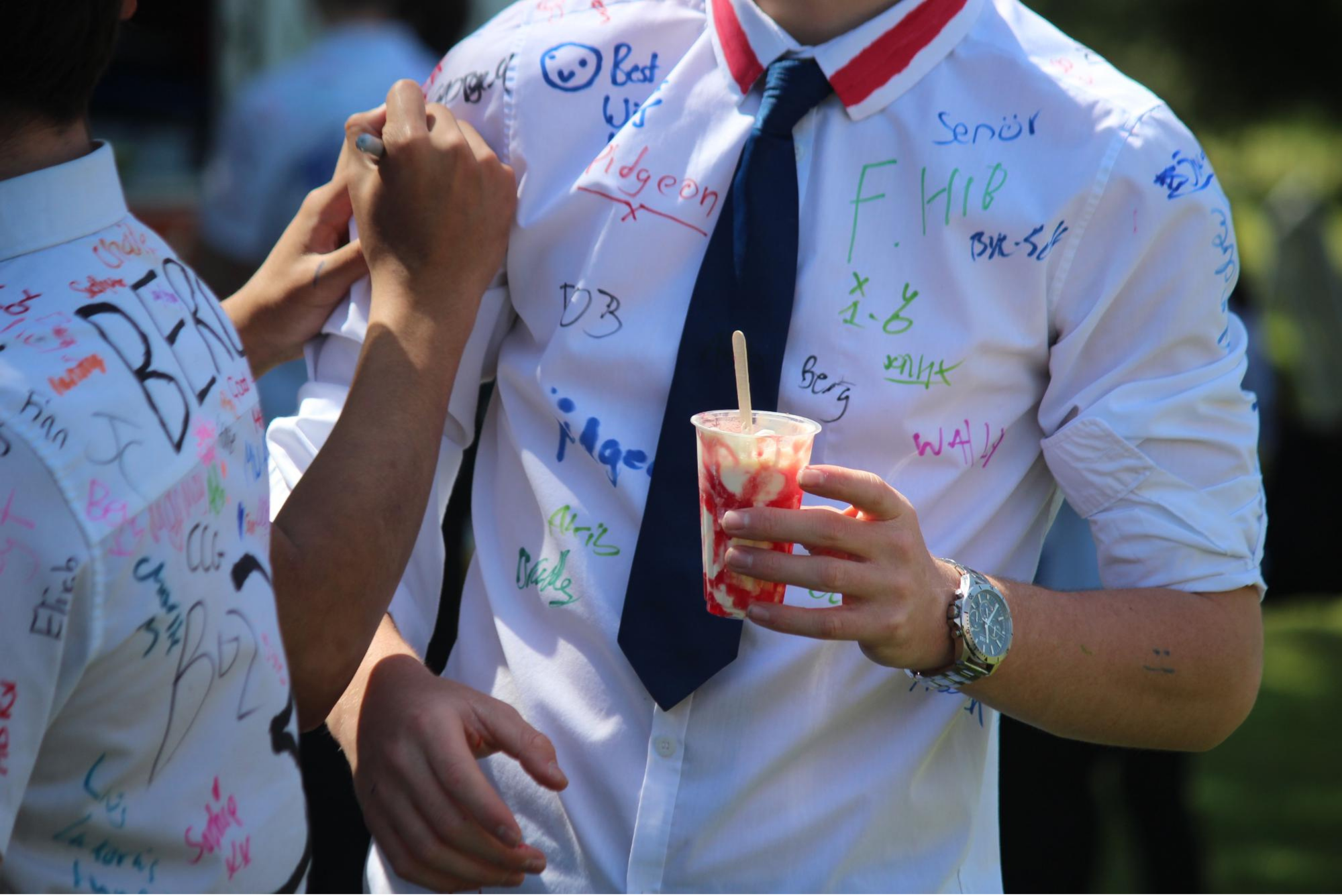 Close-up of two Year 11 pupils signing each other's shirts on leavers' day. One pupil holds an ice cream dessert.