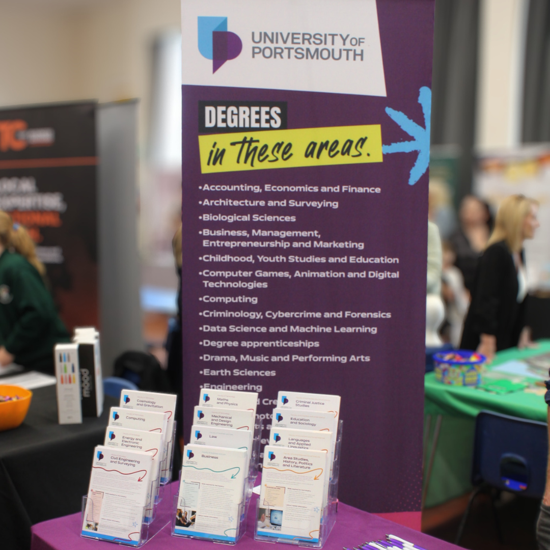 The University of Portsmouth exhibition stand featuring course information banners and subject prospectuses.