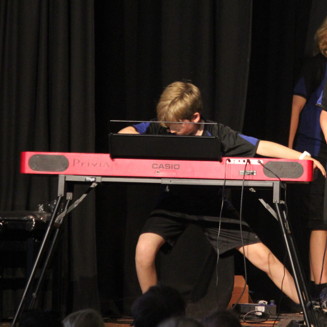 image shows a pupil dressed in PE kit enthusiastically playing the keyboard