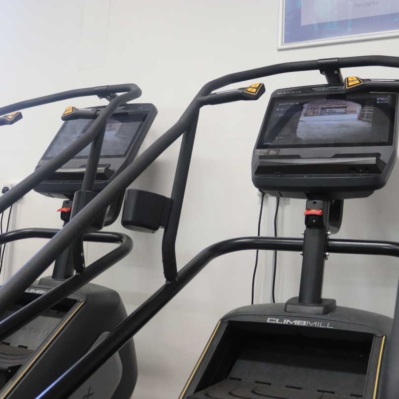 Fitness club equipment including two stair-climber machines with digital screens in a gym setting.