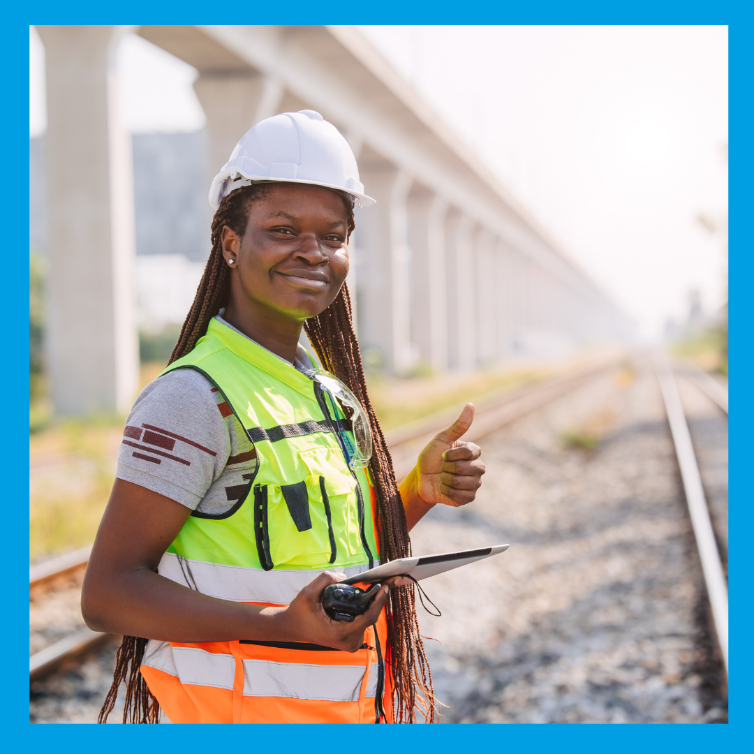 A promotional graphic set within a blue frame featuring a female railway engineer wearing a white hard hat and high-visibility vest, holding a tablet and radio while giving a thumbs-up beside train tracks