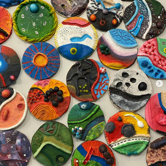 A collection of circular clay relief artworks laid out on a table, each decorated with different textures, colours, and abstract designs.
