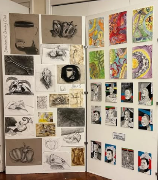 A display board showing a collection of pupil artwork, including observational drawings, mixed media studies, and colourful abstract pieces arranged in a school exhibition space.