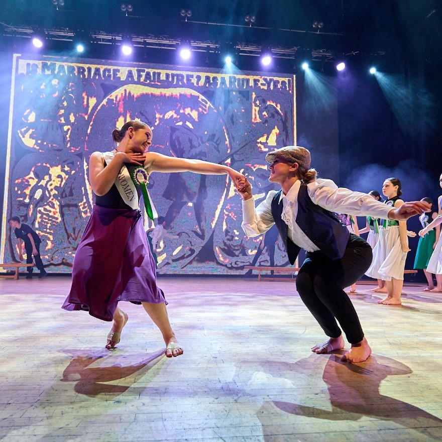 Image shows pupils taking part in a Dance Live performance with a suffrogette theme