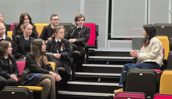 Image shows a group of pupils seated in a tiered drama studio, listening to a teacher who is seated opposite them.