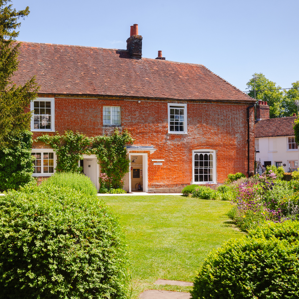 Image shows a photograph of Jane Austen's house in Chawton taken from the garden