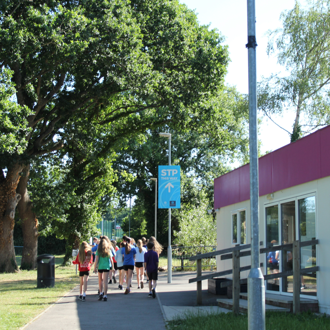 Image shows Year 6 pupils being shown around the school site, walking past trees on the edge of the school field and the RSA Hub