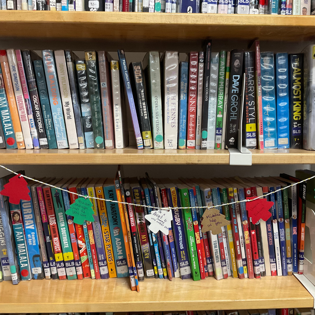 This image shows a bookcase filled with booked with a string of hand-made paper Christmas tree decorations in red green white and brown strung across it.