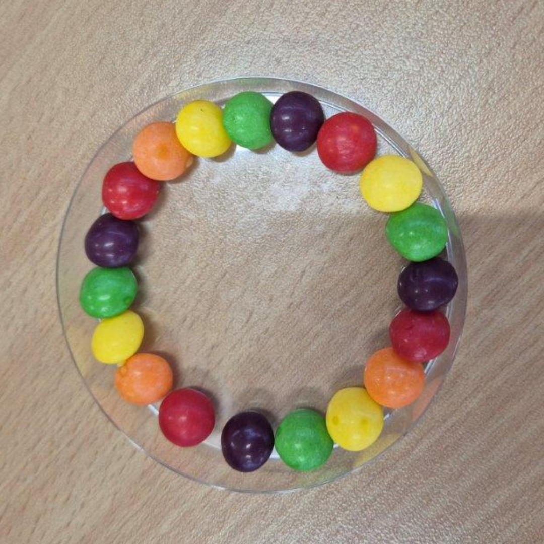 Petri dish with Skittles arranged in a neat circle before the colour diffusion reaction begins.