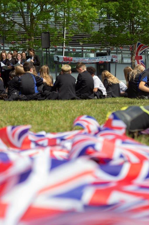 Image shows union jack bunting in the foreground, with the pupils seated on the school field enjoying the field party in the background