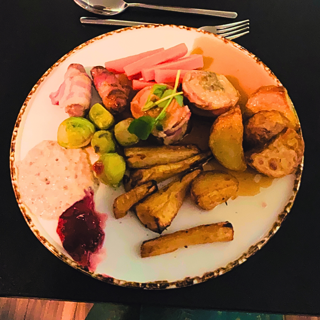 Main course plate with sliced meat, roasted potatoes, green vegetables, pickled garnish and sauce, arranged on a white plate.