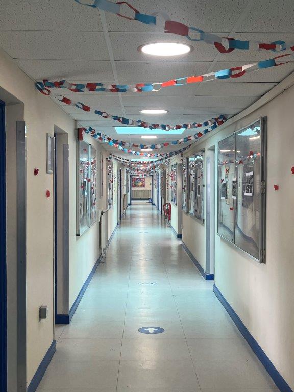 Image shows the Humanities corridor decorated for VE Day Anniversary celebrations with red, white and blue streamers, poppies, photographs and posters.