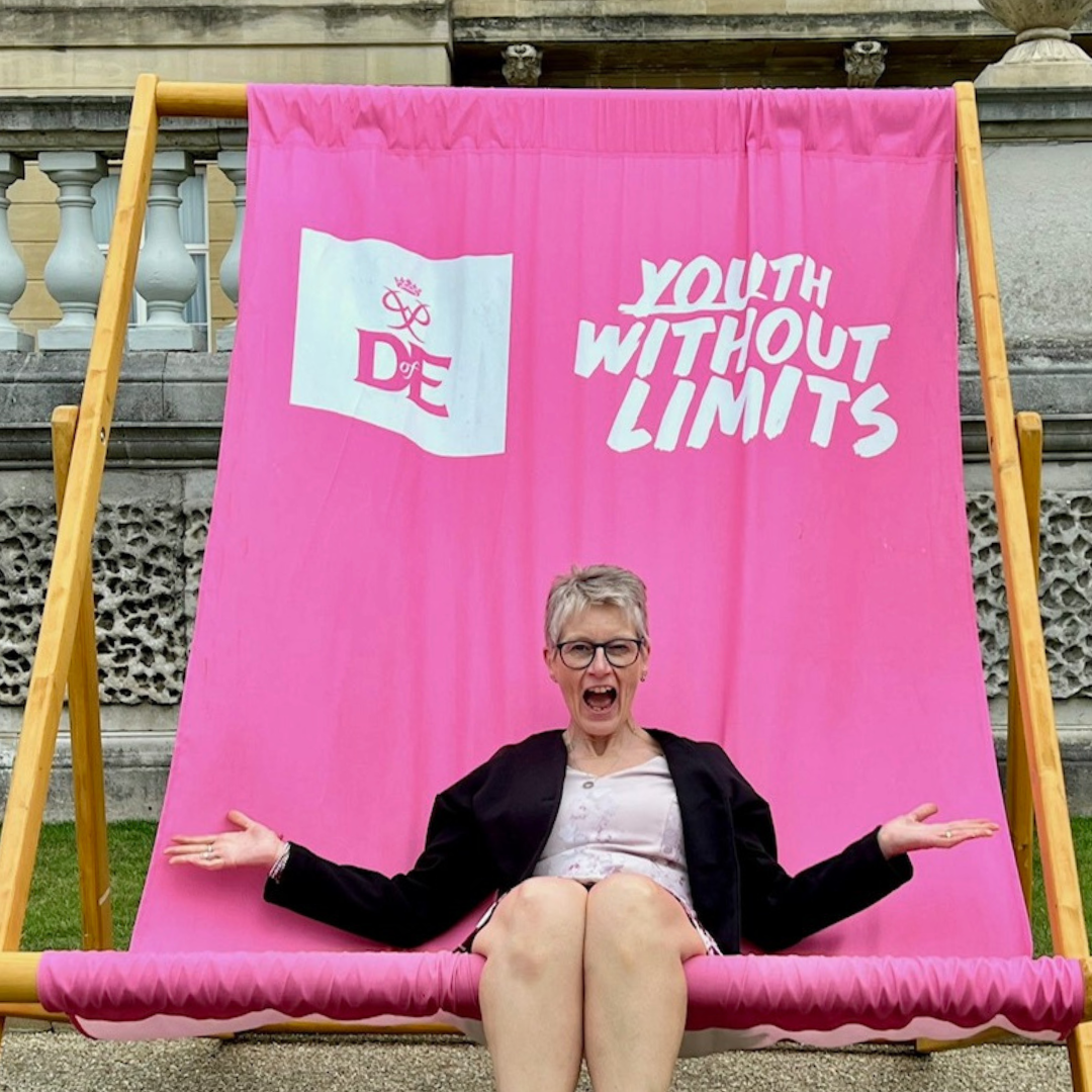 Guest sitting on a large pink deckchair featuring “Youth Without Limits” branding at the Duke of Edinburgh’s Award celebration.