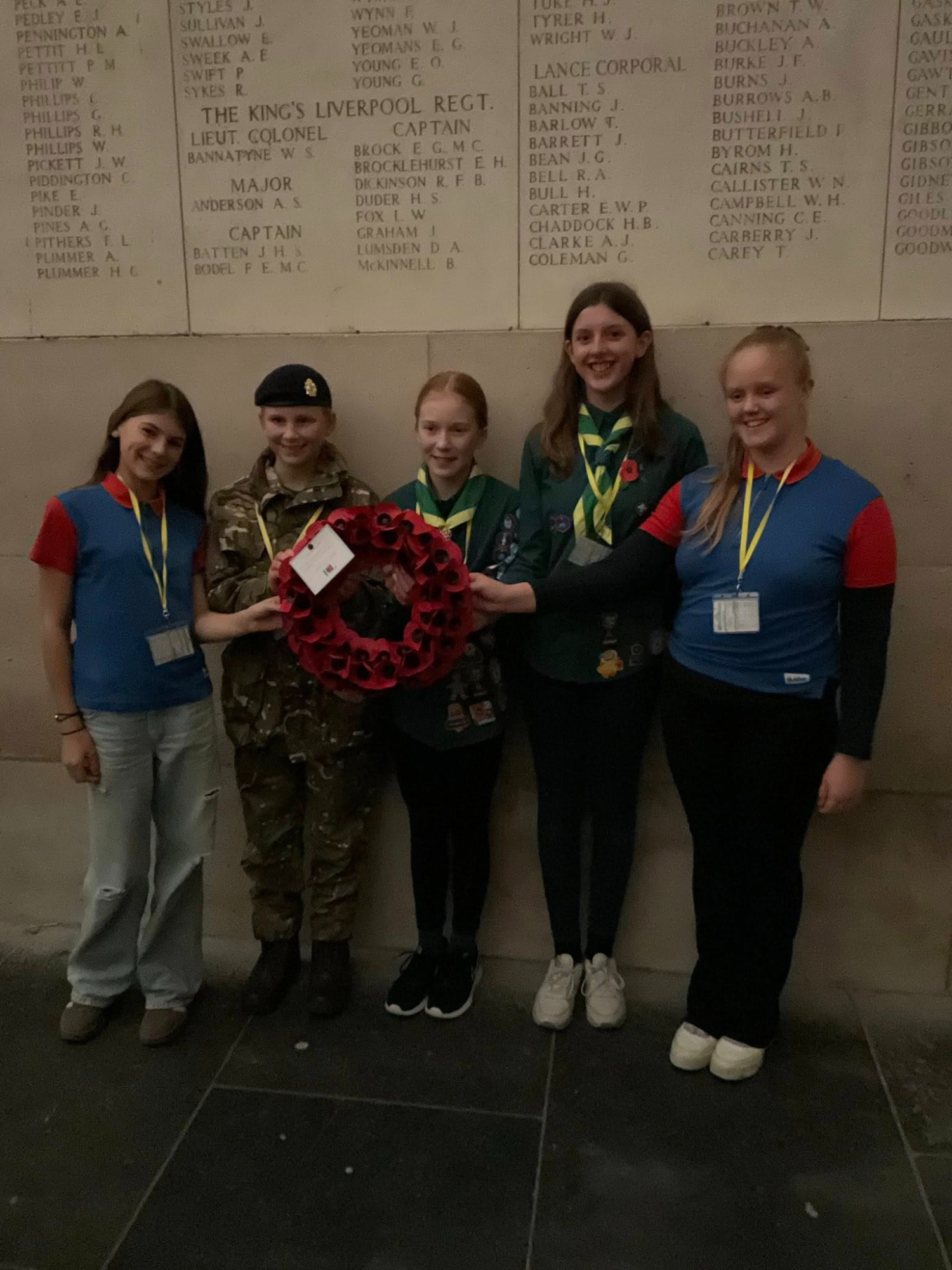 Five pupils from the College wearing various uniforms stand together holding a poppy wreath at the Menin Gate memorial.