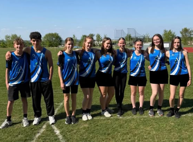 A group of Year 9 and 10 pupils wearing Swanmore College athletics kit posing together on a grass athletics field in sunny weather.
