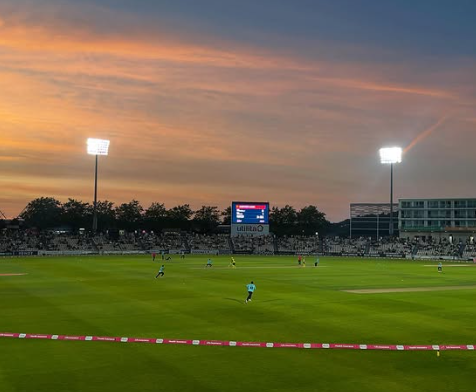 Image shows the T20 match continuing play at sunset with flood lights