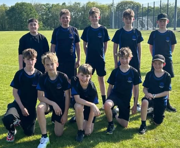 The Swanmore College Under 13 boys cricket team posing together on a grass field in PE kit on a sunny day.