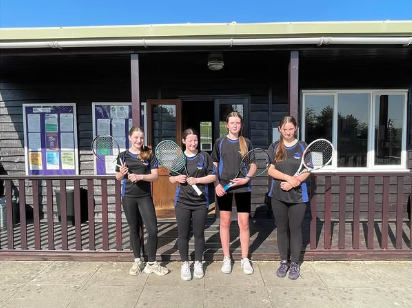 Four Year 9 and 10 girls from Swanmore College standing outside a clubhouse holding tennis rackets before a tennis fixture.