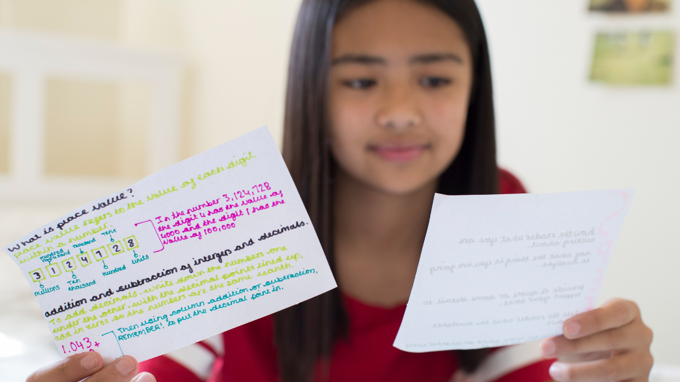 Image shows a girl using revision flash cards. We can see one of them is about place value.