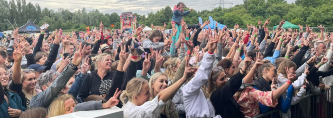 Image shows a crowd of people at a summer festive raising their hands in the air and looking like they are enjoying a live performance.