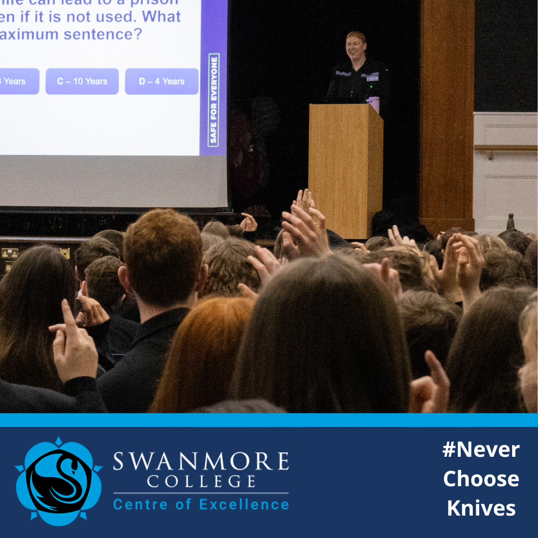 Published by Swanmore College on Wednesday, 28 January 2026. Image shows a police officer standing at a lectern in a school hall, smiling as they address a large seated audience of students. Many pupils have their hands raised to answer a question projected on a screen about knife crime and legal consequences. Swanmore College branding and the hashtag “Never Choose Knives” appear in a blue banner at the bottom of the image.