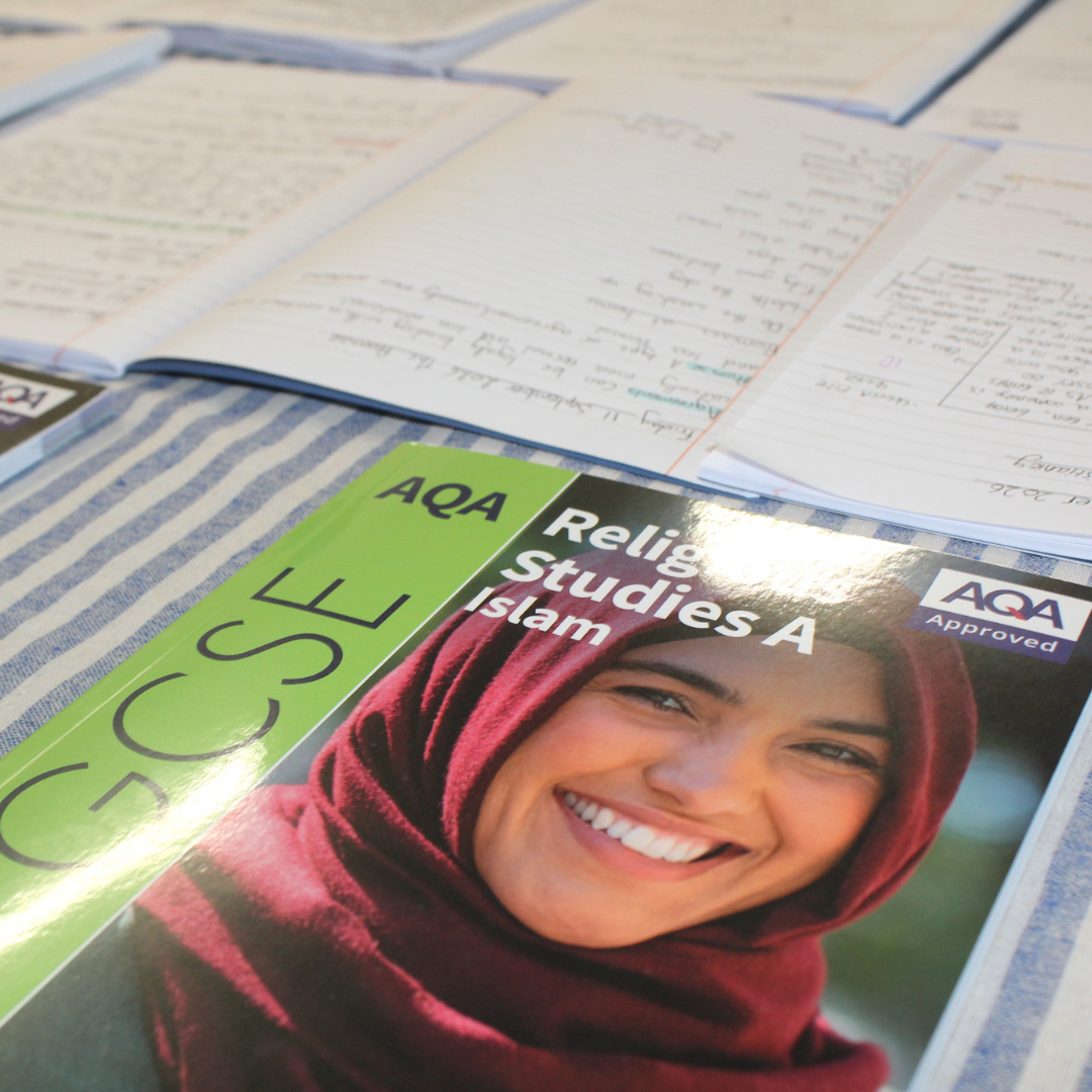 A close-up view of revision materials on a table, including open handwritten notebooks and an AQA Approved GCSE Religious Studies A Islam textbook featuring a smiling woman wearing a red hijab.